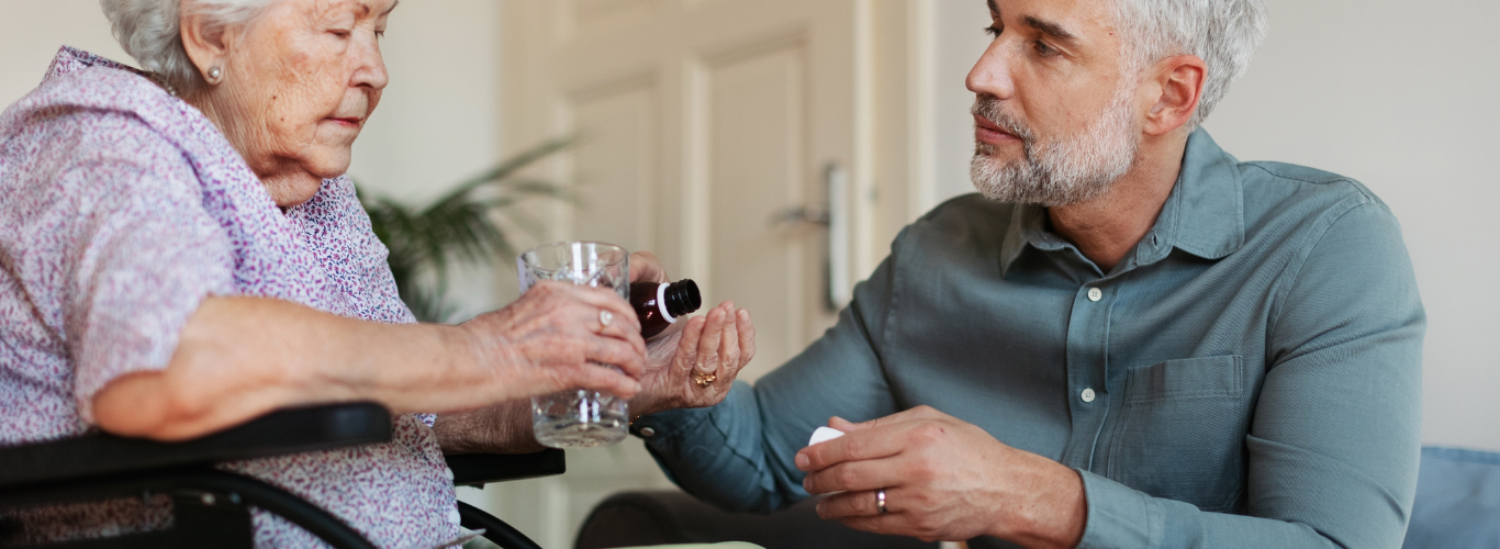 Caregiver giving medicine to older woman in a wheelchair