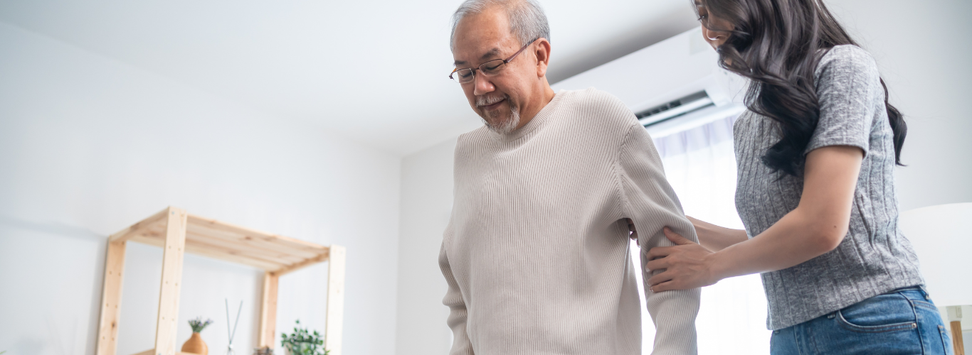 A woman assists an older man walking at home