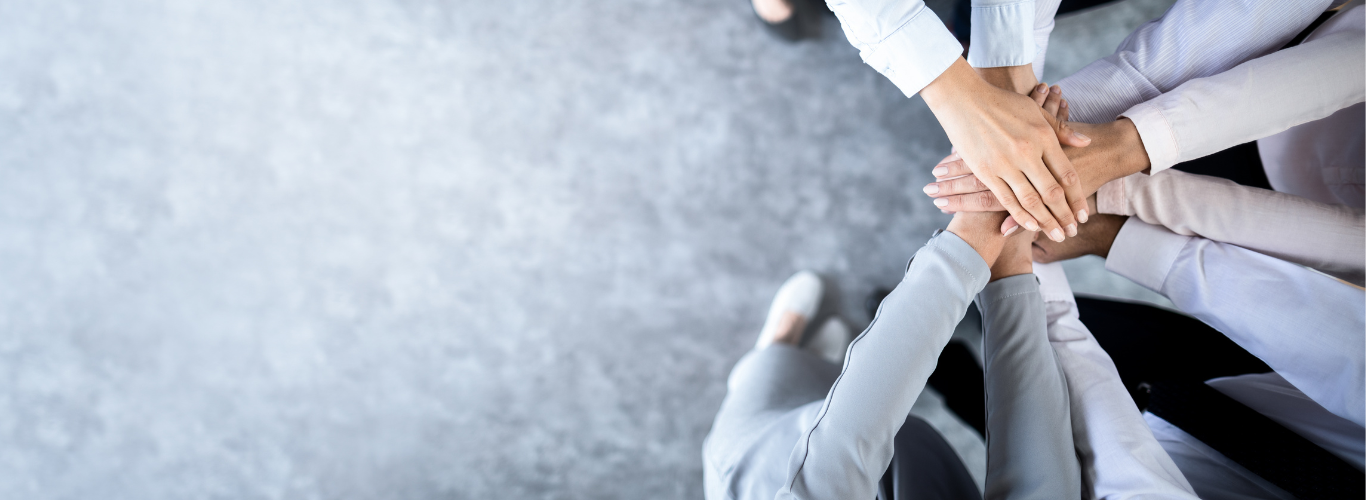 A group of professionals stand with their hands in the center of the circle